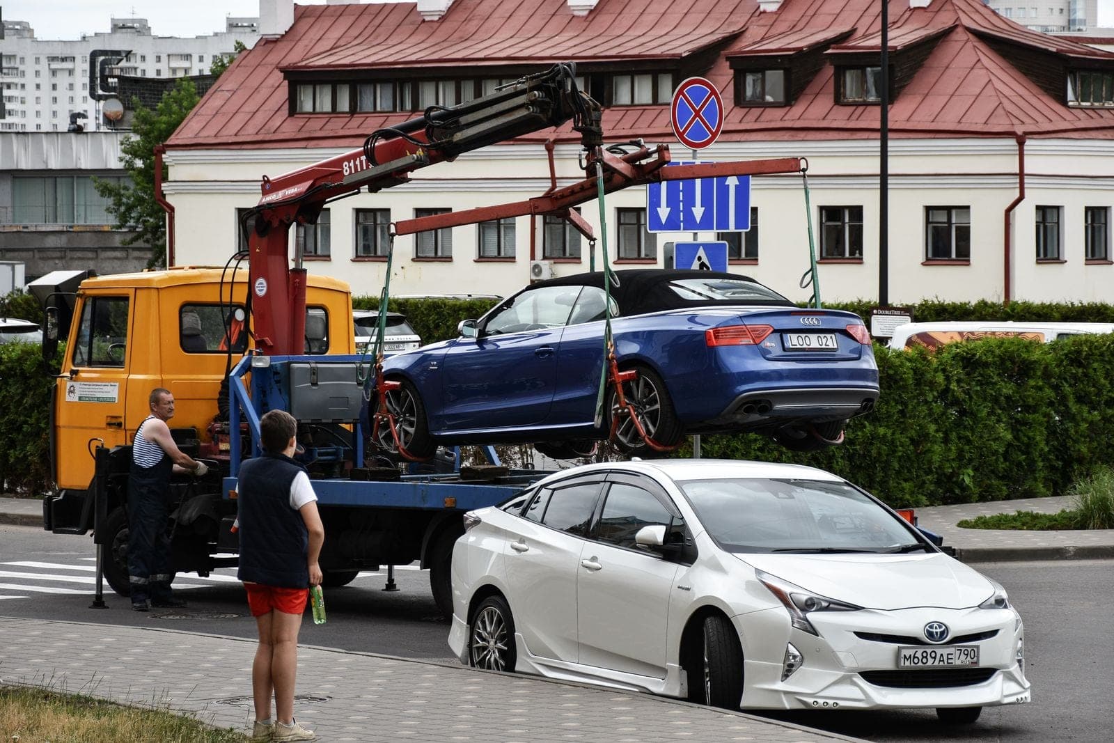 A blue convertible being lifted onto a tow truck on a city street