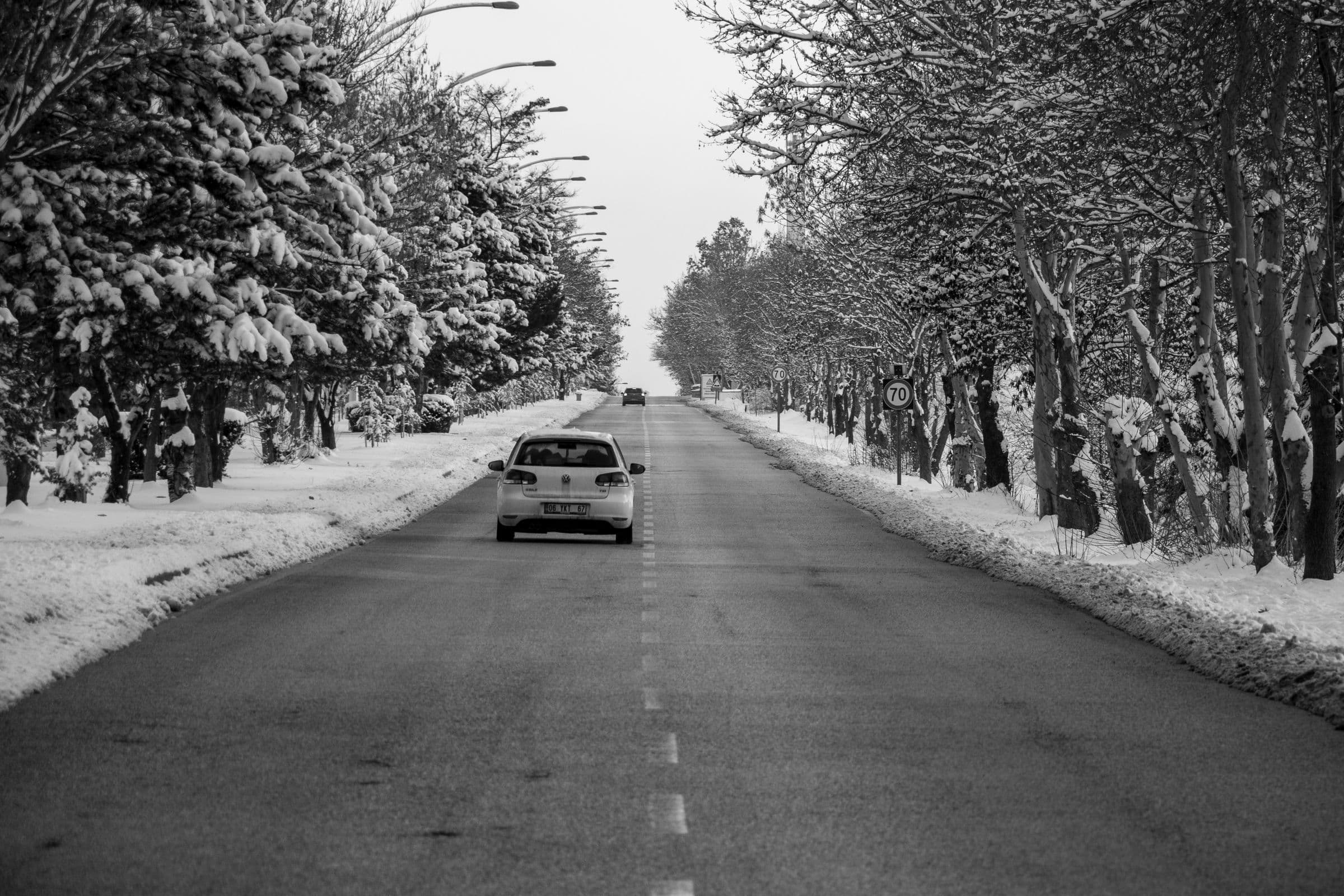A car driving down a snowy tree-lined road in winter