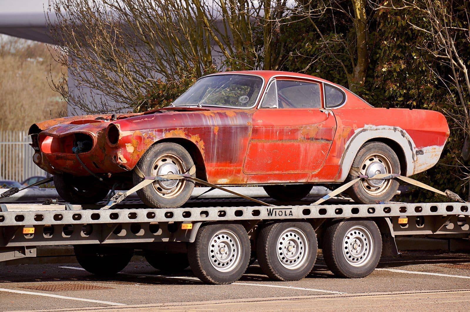 A rusty classic car strapped down on a flatbed trailer