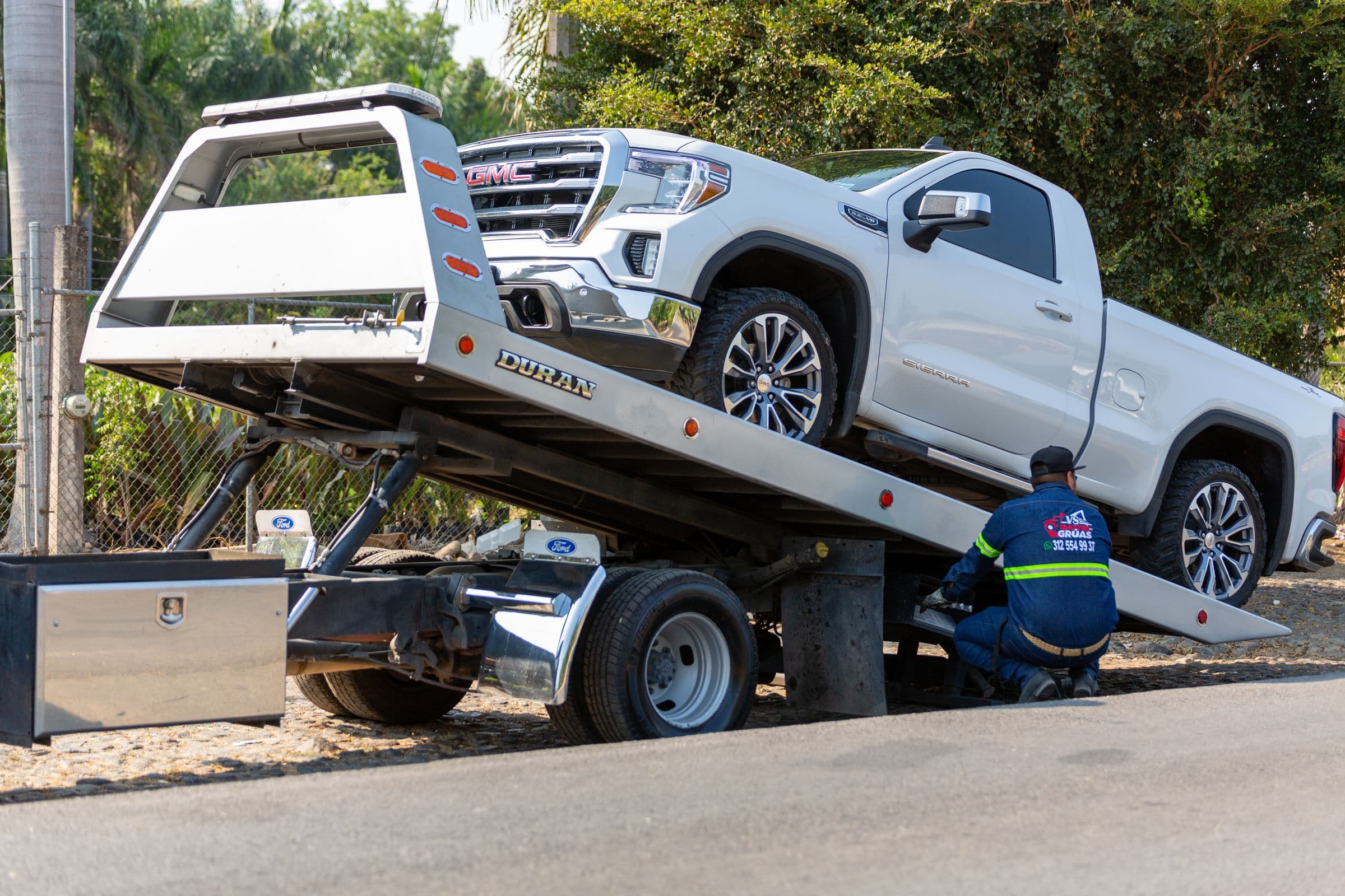 Tow operator loading a white pickup truck onto a flatbed tow truck
