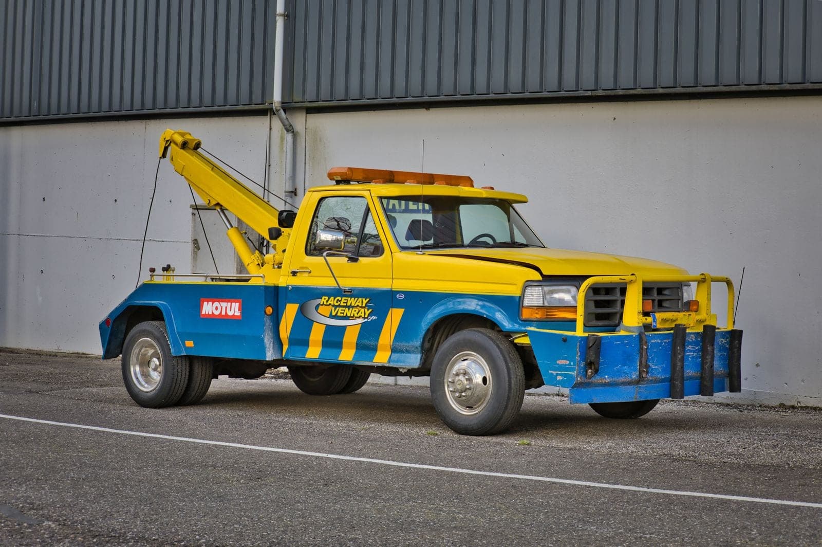 A yellow and blue tow truck with a boom parked by a building