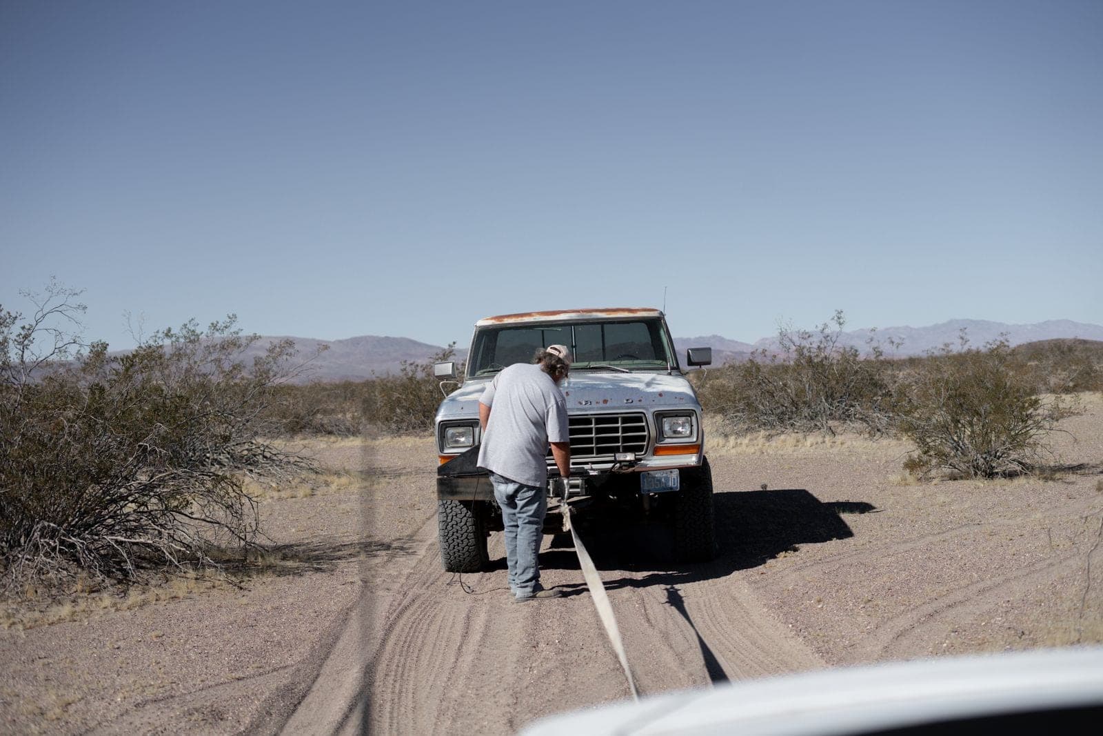 A man rigging a recovery strap to a stranded pickup truck