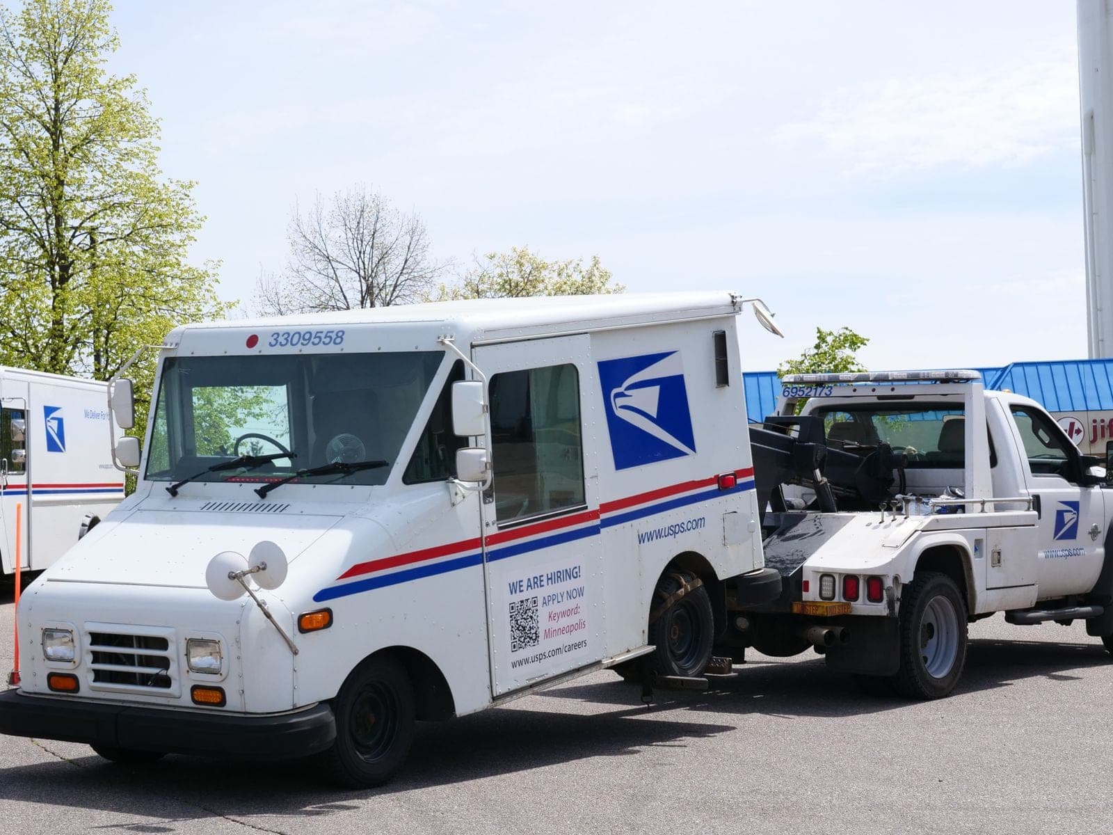 A wheel-lift tow truck towing a mail delivery truck